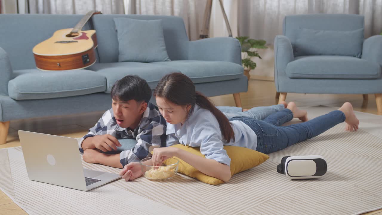 집에서 바닥에 카에 누워있는 동안 노트북을 사용하는 아시아 십대 커플의 몸이 가득 차 있습니다. 영화를 보고 간식을 먹고, 이야기하고, 함께 시간을 즐기고 있습니다.