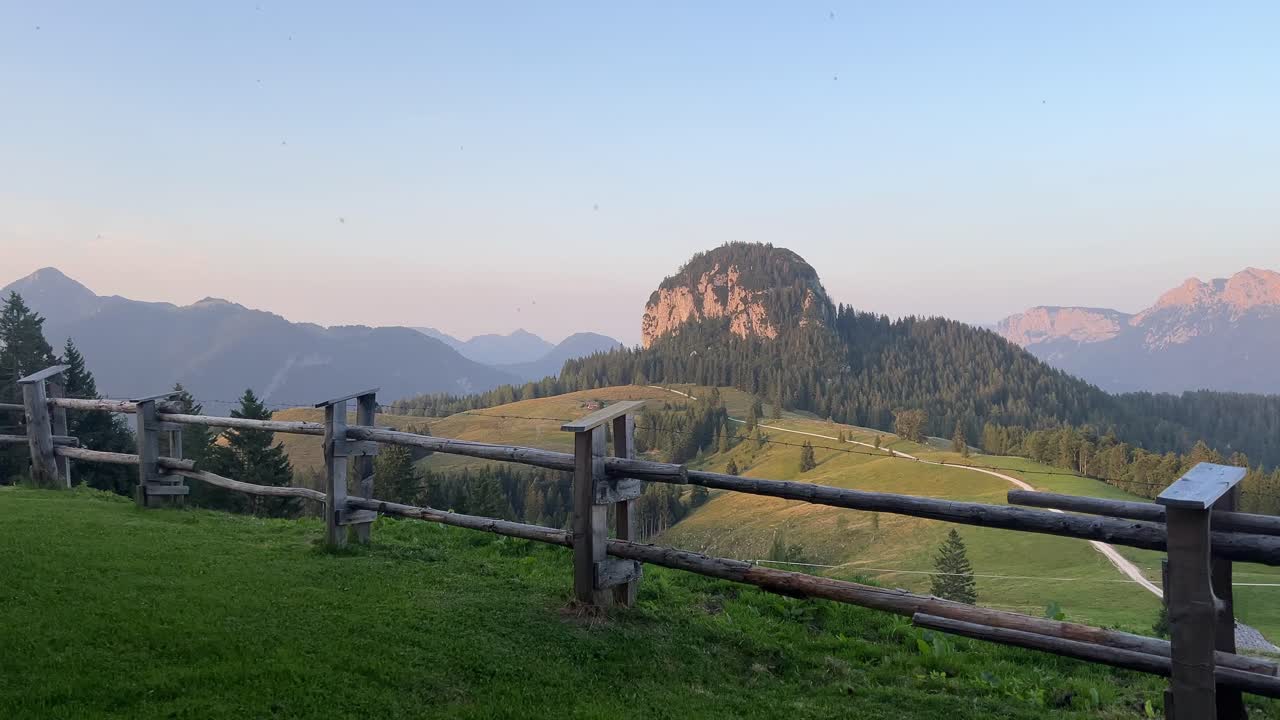 Spokojny, alpejski krajobraz o zachodzie słońca przedstawiający górę Dietrichshorn w Austrii, falujące zielone łąki, drewniany płot na pierwszym planie i miękkie wieczorne światło w Alpach