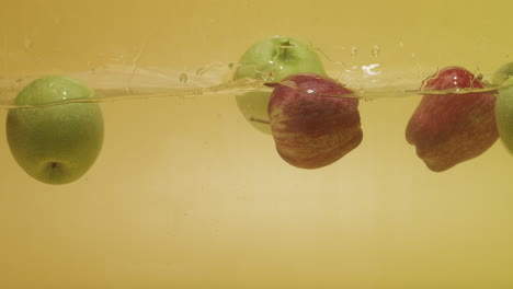 shot of a bunch of red and green apples dropped in water