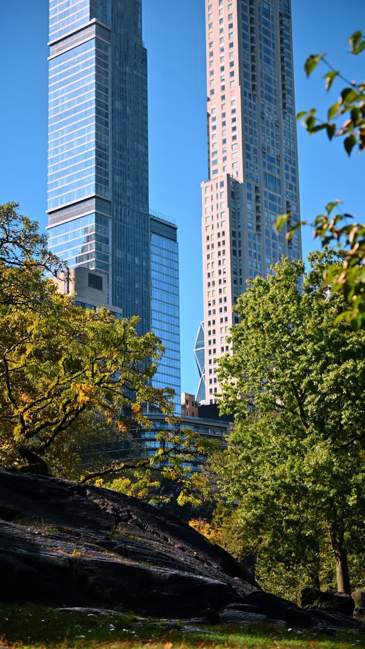 Arranha-céus de vidro da Billionaires' Row vistos do Central Park. Vista vertical de torres residenciais de luxo atrás de árvores de outono e rochas de xisto de Manhattan no Central Park