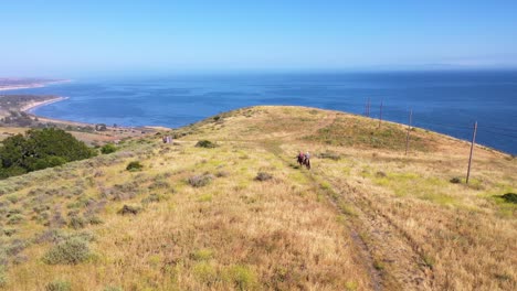 Hermosa-Antena-De-Jubilados-Pareja-De-Jubilados-A-Caballo-En-Un-Rancho-Con-Vistas-Al-Océano-Pacífico-En-Santa-Bárbara,-California