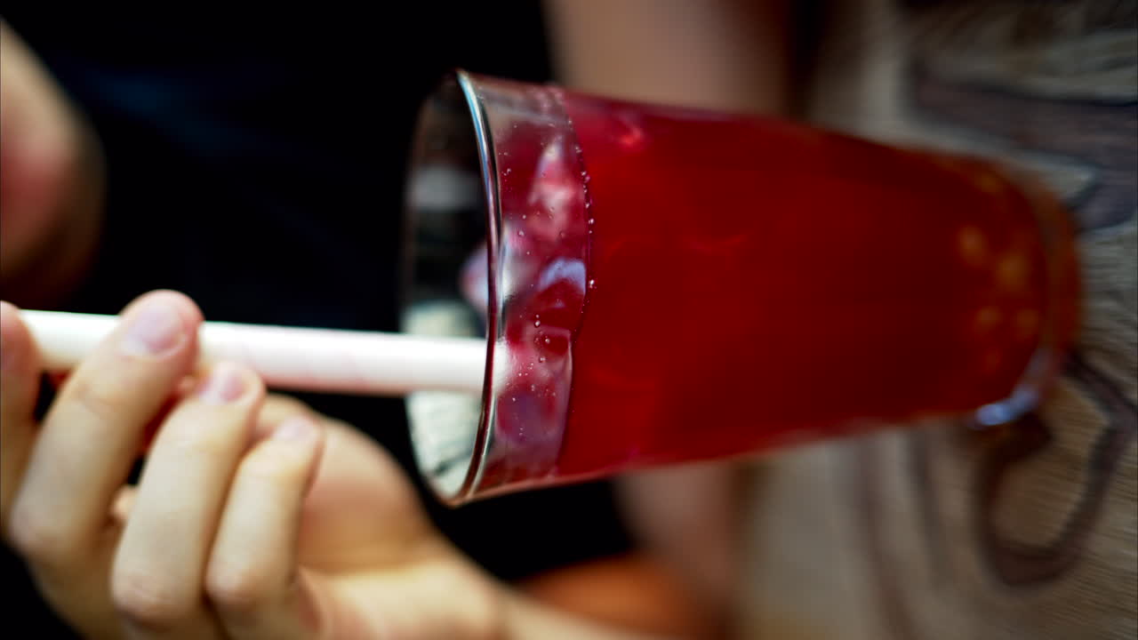 Uomo che beve bubble tea rosso con boba in un bicchiere con ghiaccio e cannuccia bianca grande, primo piano al rallentatore, schermo verticale