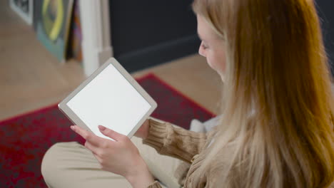 over shoulder view of young woman watching something on tablet while sitting on a couch at home