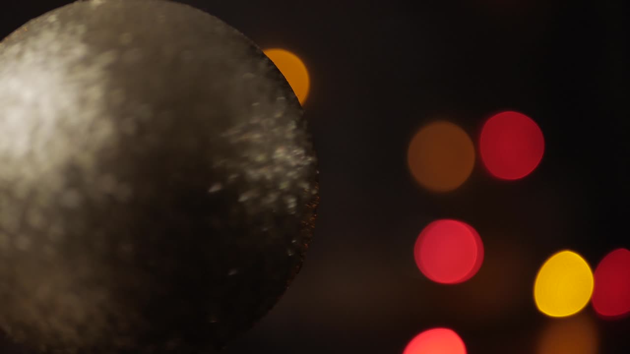 Rack focus on silver Christmas ball in foreground. Blinking Christmas lights bokeh in background. Close-up.