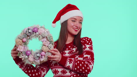 Adult-smiling-girl-in-red-Christmas-holiday-sweater-hold-raise-point-finger-on-festive-wreath-toy