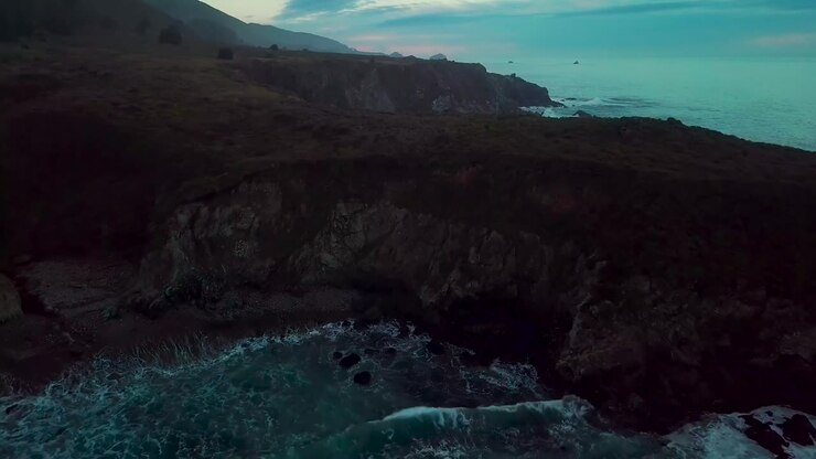 Rapida ripresa in allontanamento che rivela enormi scogliere oceaniche e onde che si infrangono a Sand Dollar Beach al tramonto a Big Sur, California