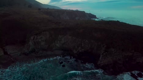 fast dolly out reveal of huge ocean cliffs and crashing waves at sand dollar beach at dusk in big sur california