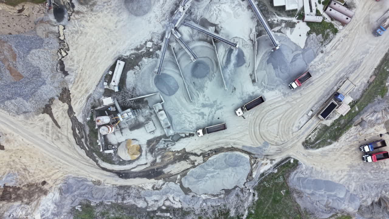 Granite quarry operation shows trucks, machinery, and raw materials at work site during daytime