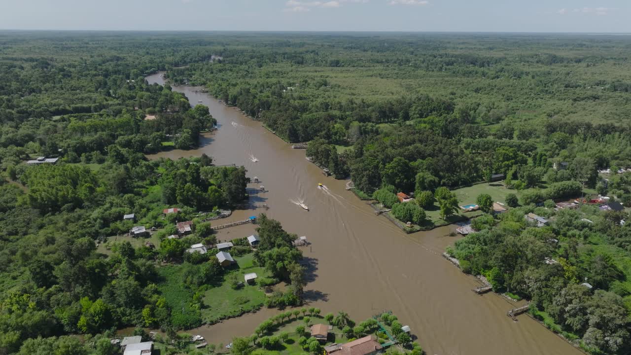 Aerial drone view: Tigre Argentina delta, winding muddy river cutting through dense rainforest canopy. Scattered homes nestled among lush vegetation. Remote jungle paradise atmosphere.