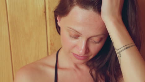 close up of thoughtful woman with closed eyes resting hand on head in calm wooden sauna setting, showing emotional introspection with natural lighting and gentle facial expression