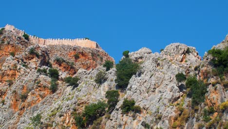 Vista-Al-Mar-De-Las-Ruinas-De-La-Antigua-Muralla-De-La-Fortaleza-Alanya-En-Un-Día-Soleado-De-Verano,-Cielo-Azul-Claro,-Tiro-De-Mano-Medio-Desde-Un-Barco