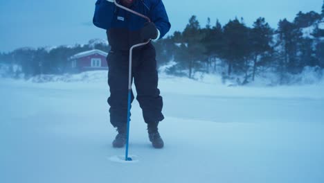 man drilling hole in frozen lake for ice fishing - close up