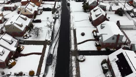 an aerial view over a quiet, suburban neighborhood after a snow storm with the area covered with snow on a cloudy day