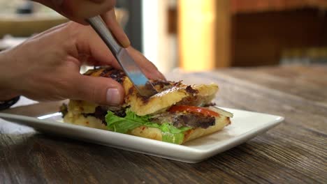 caucasian man cutting beef sandwich for breakfast at stylish cafe