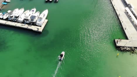 Aerial-tracks-motorboat-entering-vivid-green-marina-on-Majorca,-Spain
