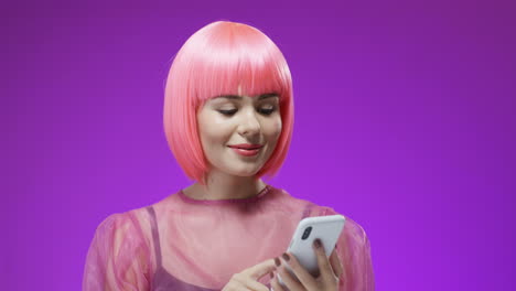 mujer bonita con una peluca rosa tocando y enviando un mensaje de texto en su teléfono inteligente