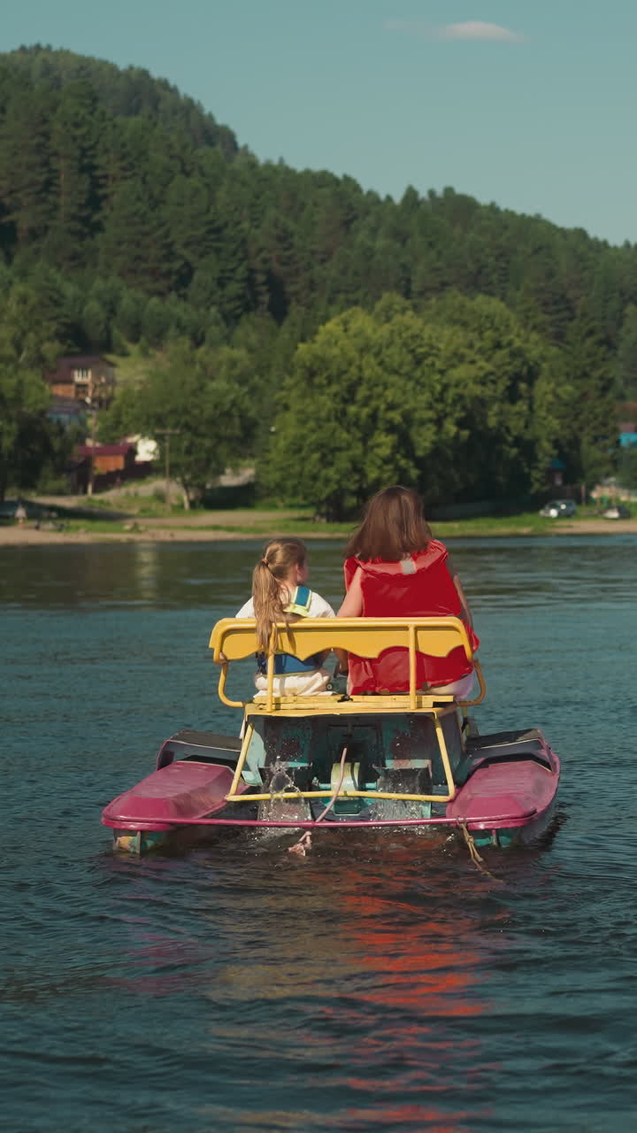 Couple of sisters sits in catamaran on river looking at speedboat. Active pastime on weekends slow motion. Tourists have fun on water transport backside view