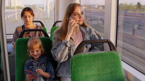 Parent-mother-talking-on-mobile-phone,-ignoring-little-child-daughter-while-sitting-in-public-tram