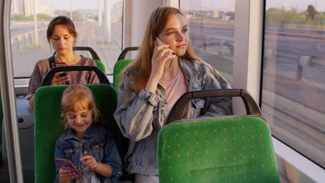 parent mother talking on mobile phone, ignoring little child daughter while sitting in public tram