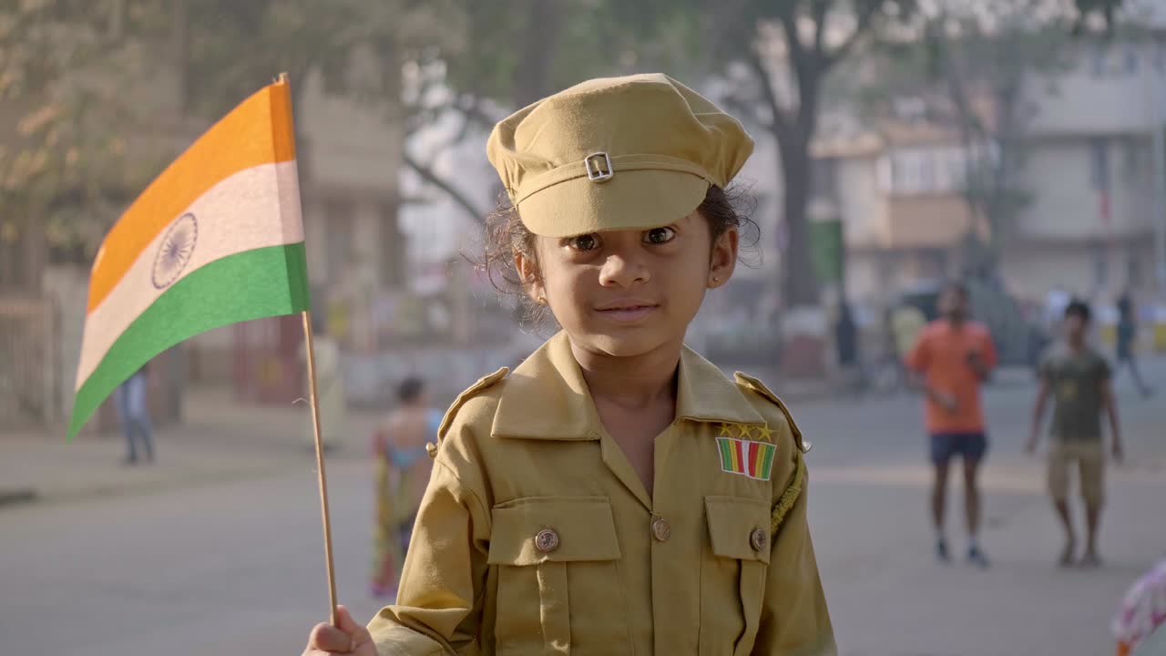 Una giovane ragazza sorridente, felice e carina in uniforme da soldato e che tiene in mano una bandiera nazionale indiana, tricolore