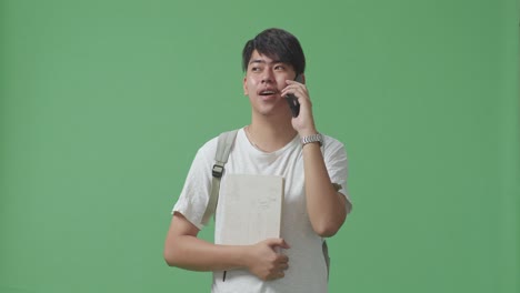아시아인 학생이 녹색 스크린 스튜디오에서 휴대전화로 이야기하고 있습니다.