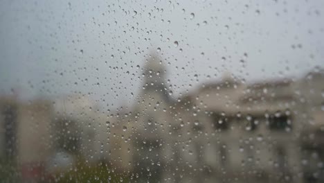 Imágenes-Estrechas-En-Cámara-Lenta-De-Gotas-De-Lluvia-Vistas-A-Través-De-Una-Ventana-Durante-Fuertes-Lluvias,-Con-Un-Paisaje-Urbano-De-Fondo