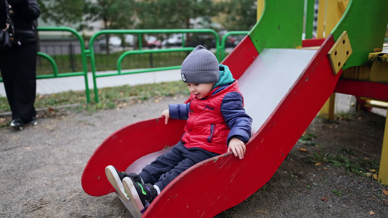 Lovely baby sitting on the slide. Cute toddler slides down smiling sweetly. Kid on the playground in autumn.