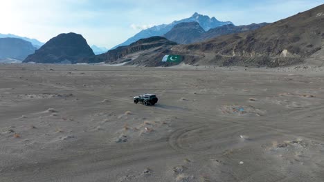 off-road vehicle traversing sarfaranga cold desert with a pakistan flag in skardu valley