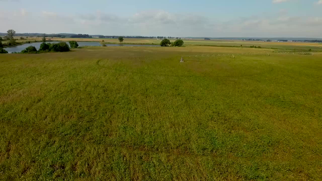 arial bajo de tierras de cultivo volando hacia un estanque en un día soleado