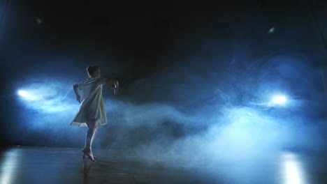 Modern-ballet-dancing-woman-barefoot-doing-spins-and-pirouettes-and-dance-steps-standing-on-stage-in-smoke-in-slow-motion.-Performance-on-stage.