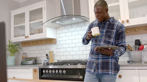 African-american-man-using-tablet-and-drinking-coffee-in-kitchen-at-home,-slow-motion