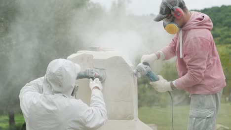 two sculptors create a statue of stone with a hammer and grinder