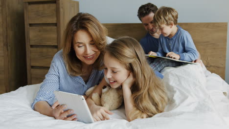 vista de cerca de una niña y su madre acostadas en la cama y viendo algo en la tableta