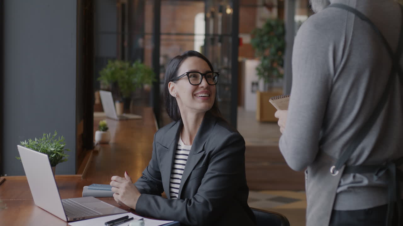 Businesswoman having a conversation with a waiter in a modern office cafe.
