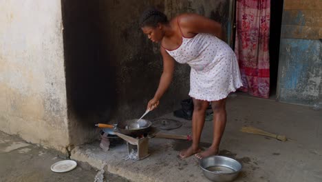 barefoot black african woman cooking outside her house, frying fish to accompany banku, ghana national dish