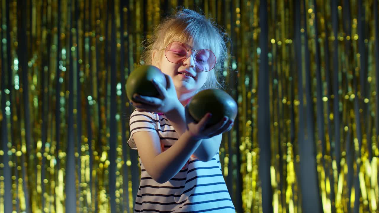 화려한 배경에 서 있는 망고 과일을 가진 세련된 귀여운 십대 소녀가 춤을 추고 우스스럽게 놀고 있습니다.