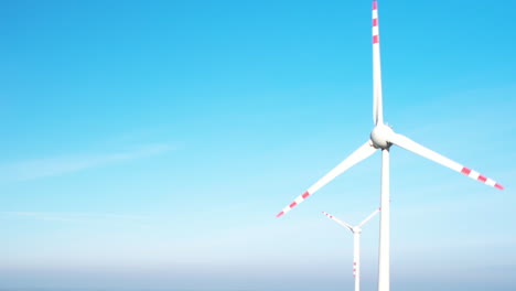 White-and-red-wind-turbines-spinning-against-blue-sky-background-in-Poland---aerial-close-up-orbiting