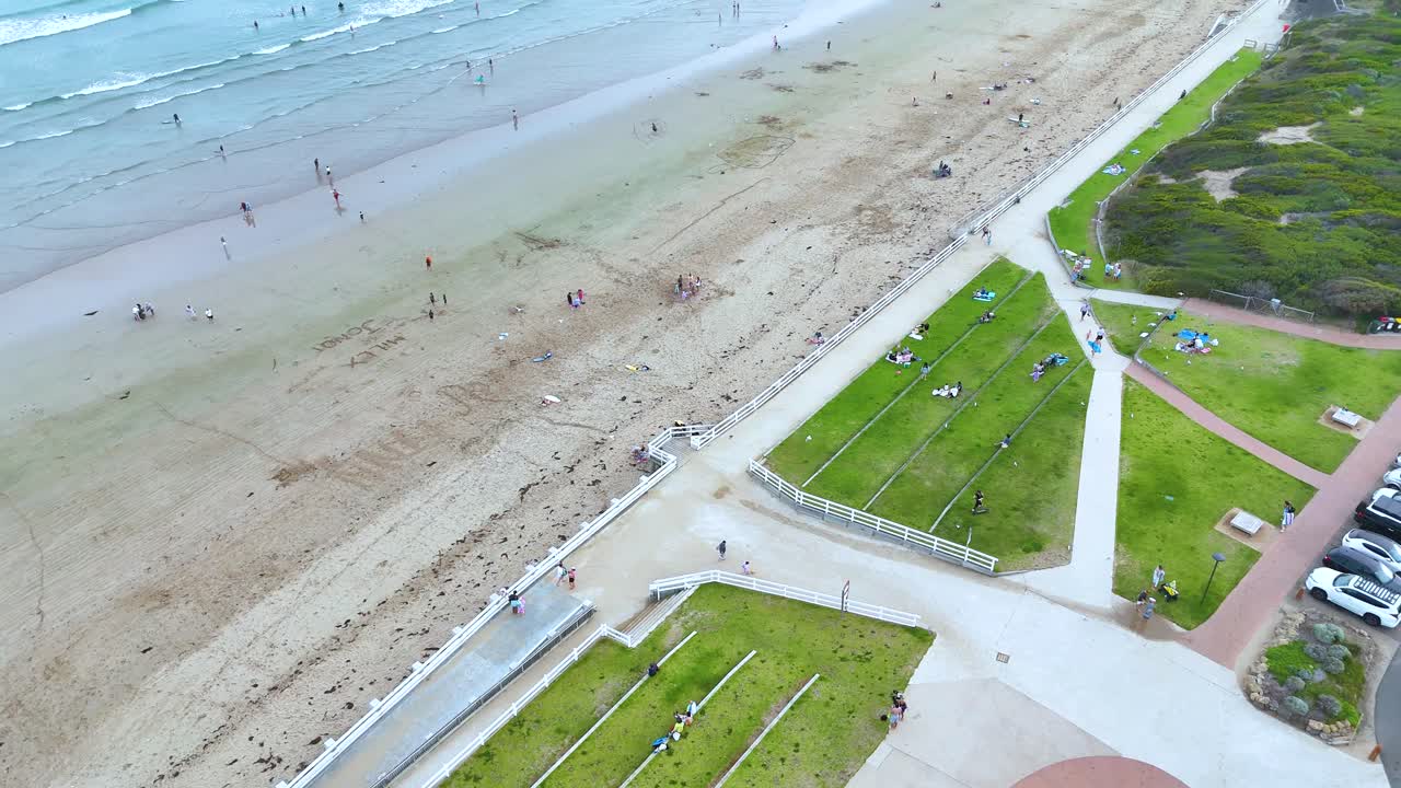 Aerial footage captures people enjoying a sunny day at Ocean Grove Beach, Victoria, showcasing vibrant green spaces and ocean waves