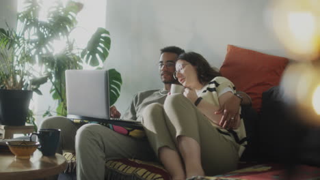 couple cuddling on sofa and using laptop