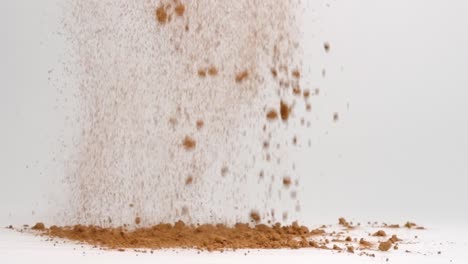 chocolate brown cocoa powder ingredient for baking falling into pile on white table in slow motion