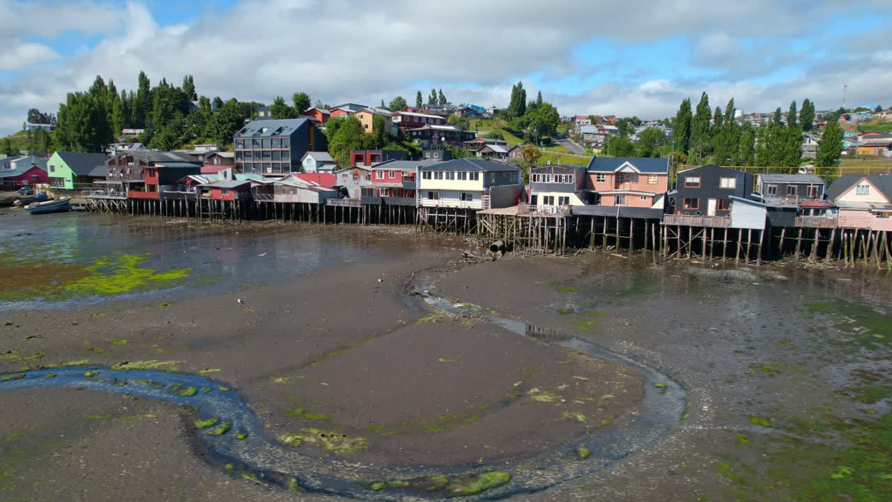 Colorful stilt houses on a cloudy day in Castro, Chiloé, showcasing low tide, vibrant culture, and local architecture