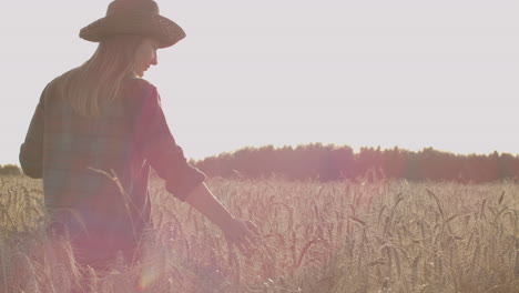 Young-girl-farmer-in-plaid-shirt-in-wheat-field-on-sunset-background.-The-girl-uses-a-tablet-plans-to-harvest.