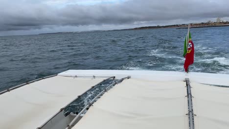 portuguese flag flying on the back of boat sailing on a gloomy day