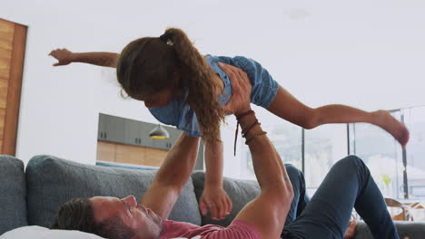 father playing game with daughter lying on sofa and lifting her in the air