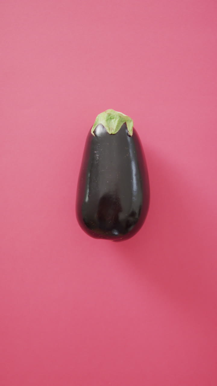 Vertikal video med hög vinkel av färsk aubergine på rosa bakgrund