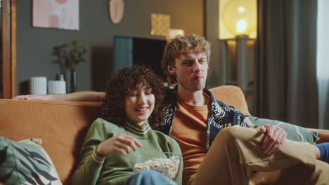 young couple watching movie together on comfortable sofa at home