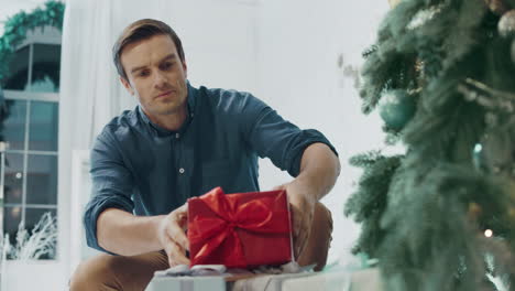 Schöner-Mann,-Der-In-Einem-Luxushaus-Ein-Geschenk-Unter-Den-Weihnachtsbaum-Legt