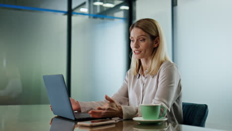 Smiling-woman-greeting-at-video-chat-in-office-close-up.-Happy-director-waving