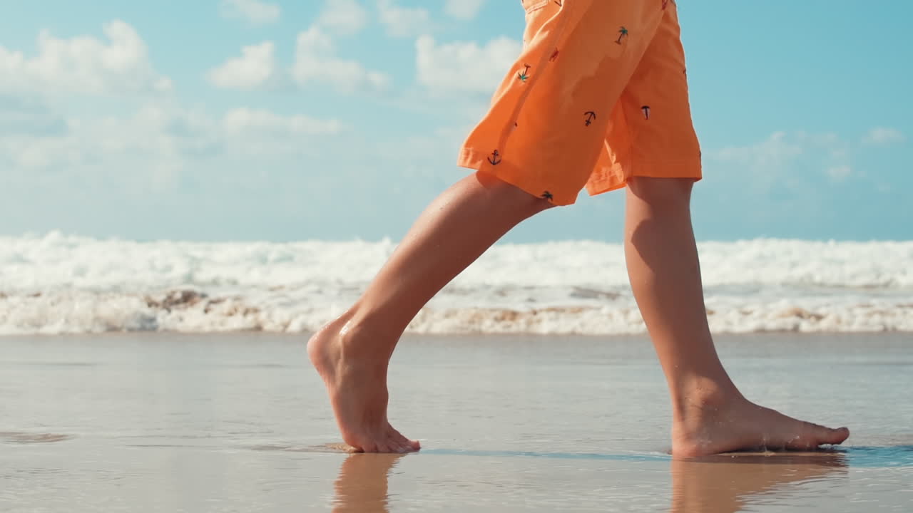 Adolescente sconosciuto che cammina sulla spiaggia. Le gambe del ragazzo lasciano impronte sulla battigia.