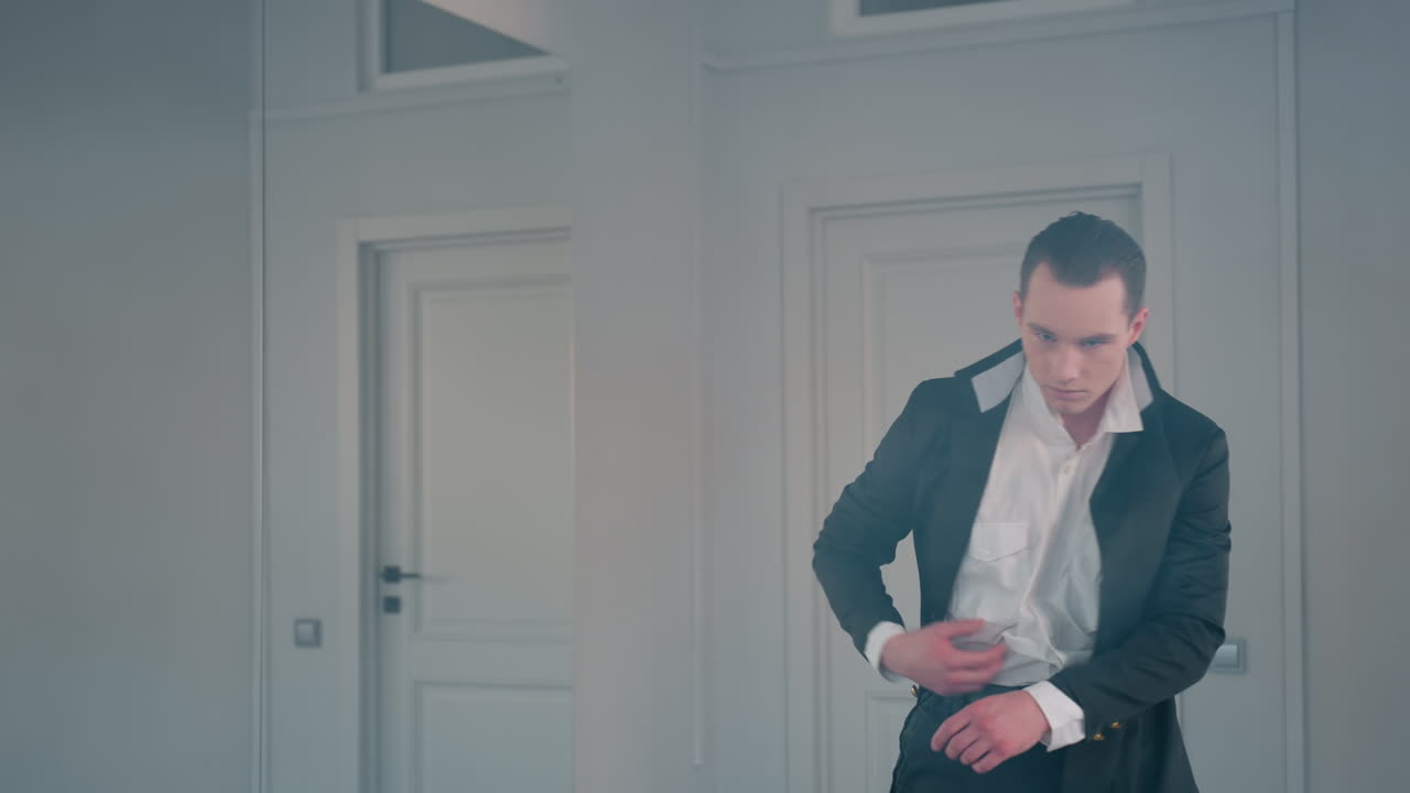 elegant man in black coat and white shirt dances gracefully in smoke filled room with dramatic lighting, showcasing fluid movement, stylish attire, and artistic performance in minimalist setting